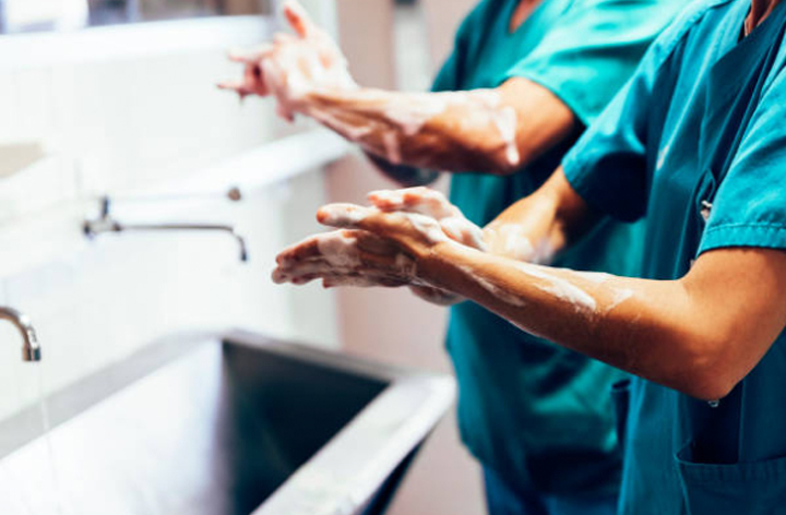 Two medical professionals in scrubs are washing their hands with soap at a sink, following proper hygiene procedures.