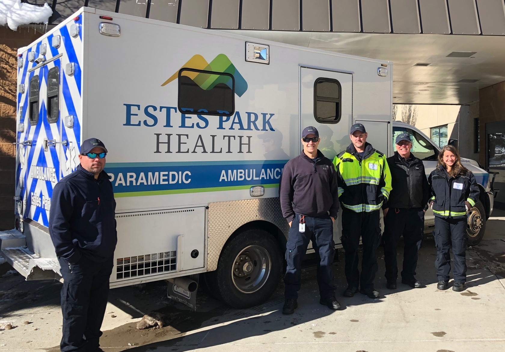 Five paramedics wearing uniform stand in front of an Estes Park Health ambulance parked outside a building.