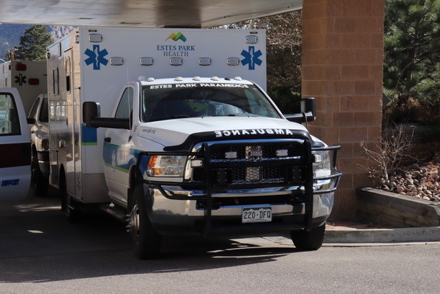 An Estes Park Health ambulance is parked underneath an awning, with another emergency vehicle partially visible in the background.