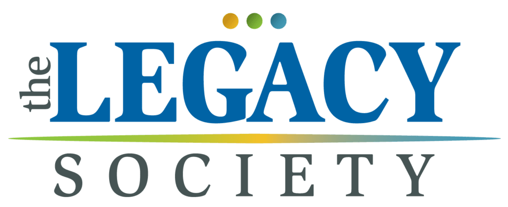 Logo for The Legacy Society with blue text. A colored gradient line runs beneath the text, and three small circles (yellow, green, and blue) are above the word "LEGACY".