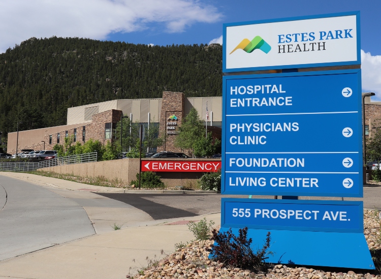 A large blue sign outside Estes Park Health with directional information for the hospital entrance, physicians clinic, foundation, living center, and emergency, located at 555 Prospect Ave.