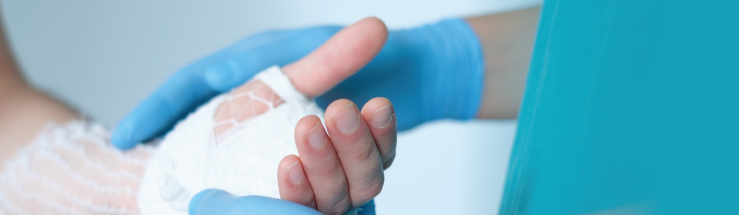 A medical professional in blue gloves holds the hand of a patient with a bandaged wrist and wrapped hand, providing care or support.