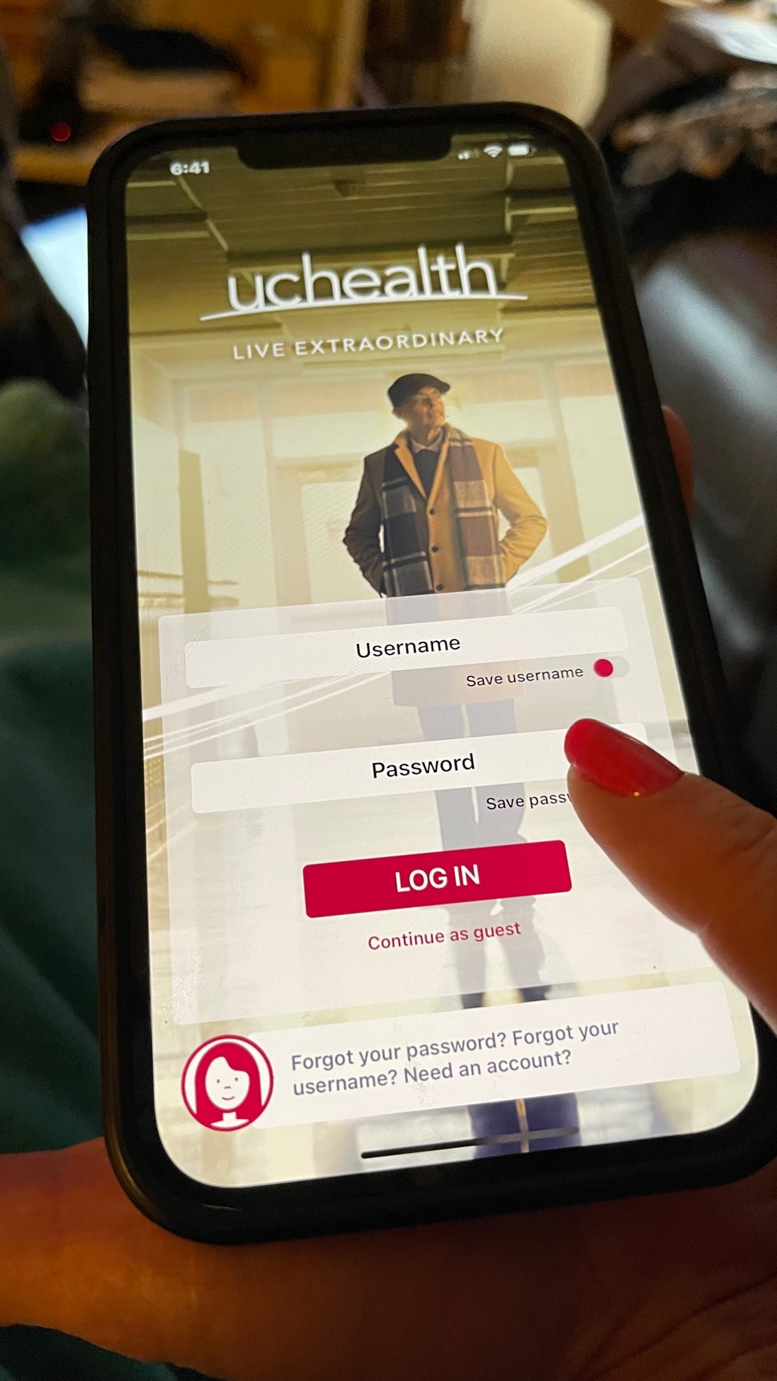 A person is holding a smartphone displaying the UCHealth app login screen, with fields for username and password and options to save credentials or continue as a guest.