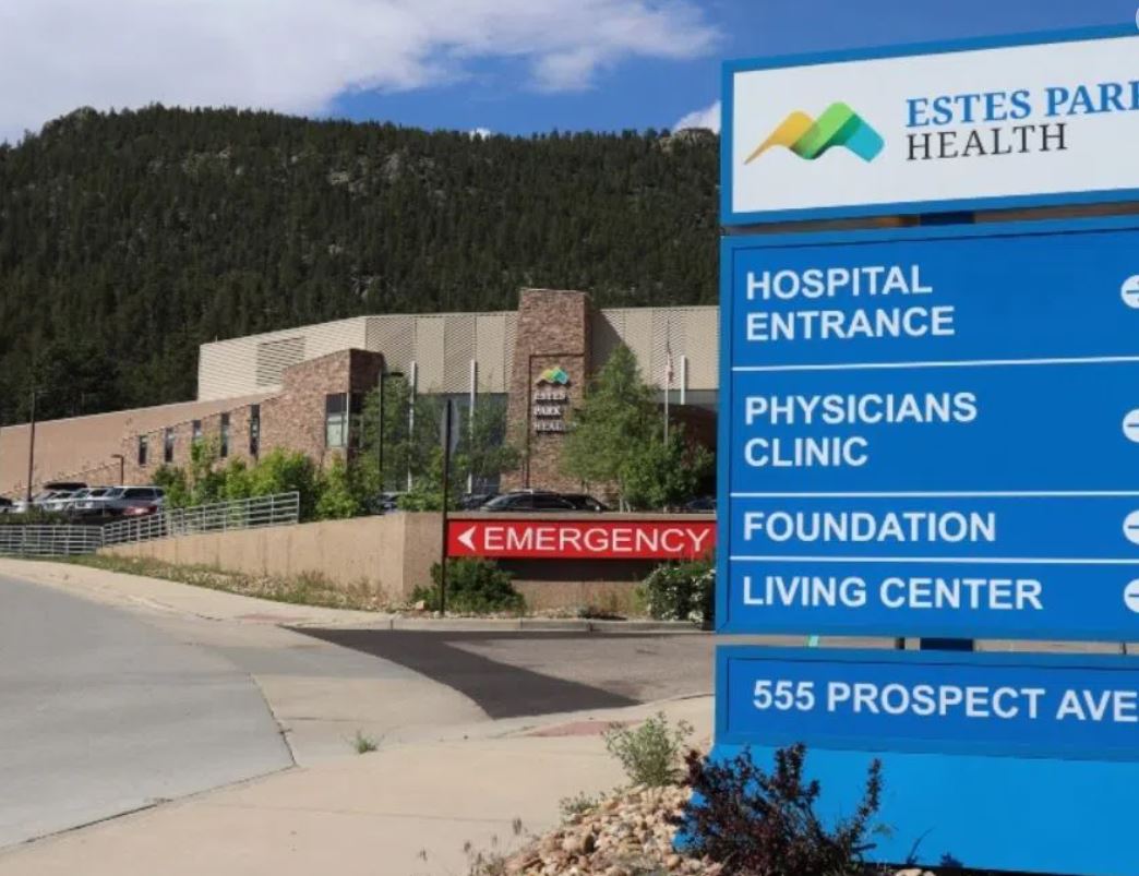 Image of Estes Park Health facility with a directional sign in the foreground indicating locations such as hospital entrance, physicians clinic, foundation, living center, and emergency.