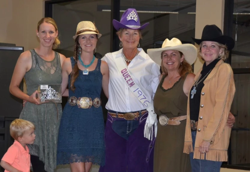 Five women, dressed in Western attire, stand side by side smiling, with the woman in the center wearing a sash that reads 