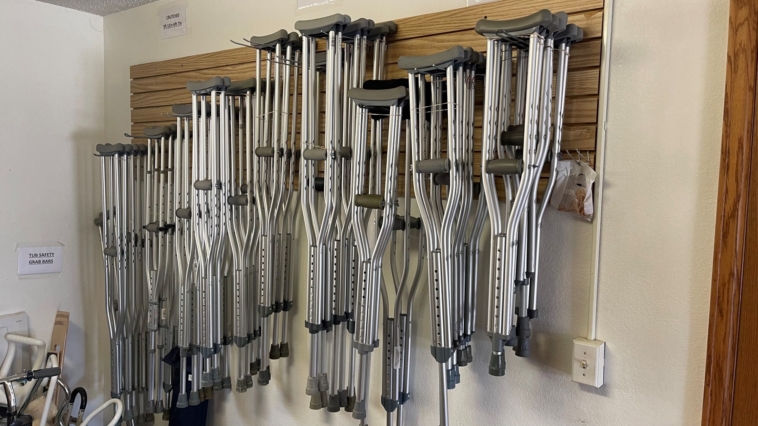 A variety of crutches are neatly organized and hanging on a wall-mounted rack inside a room.