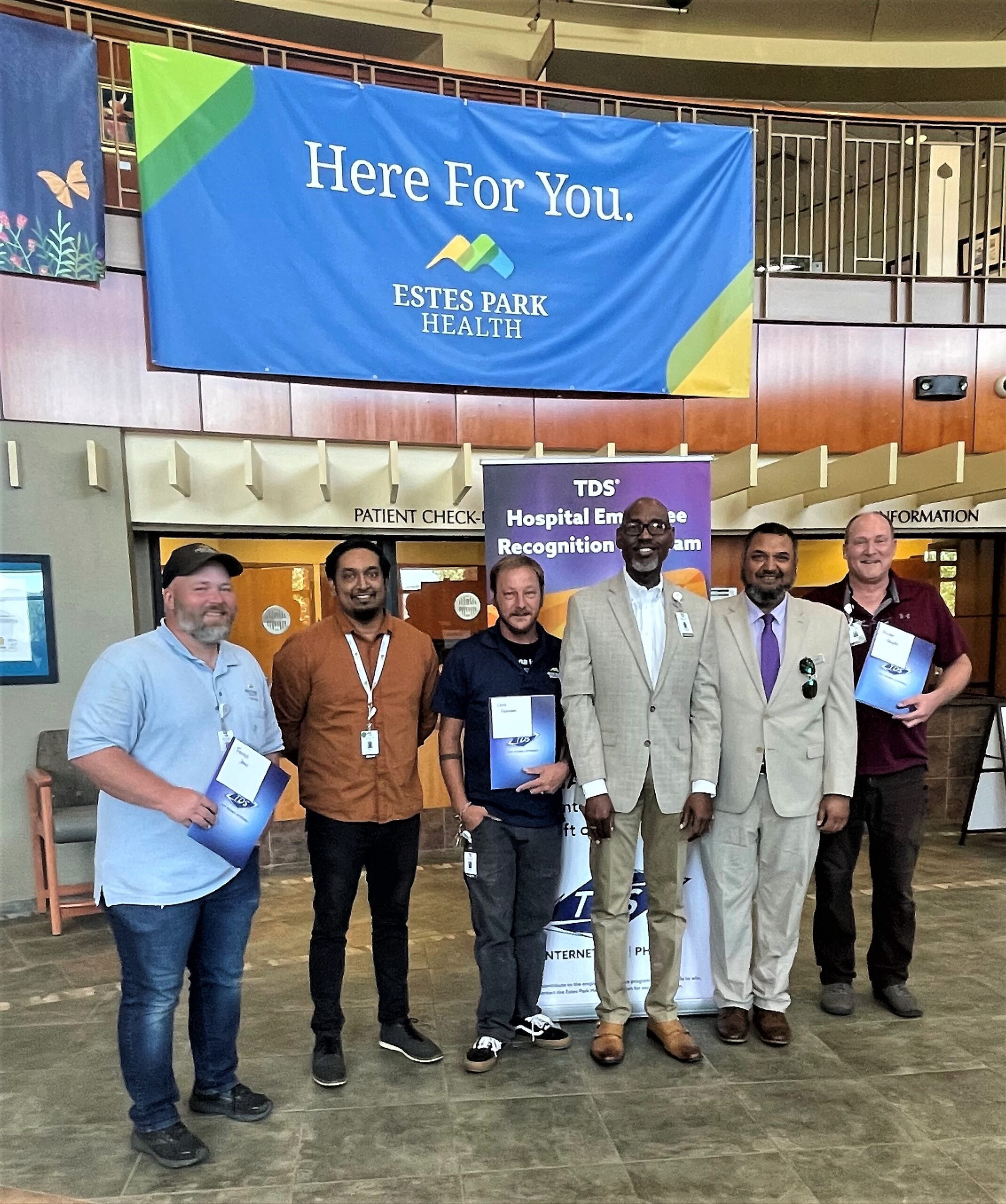 Six people are standing indoors in front of a banner that reads 