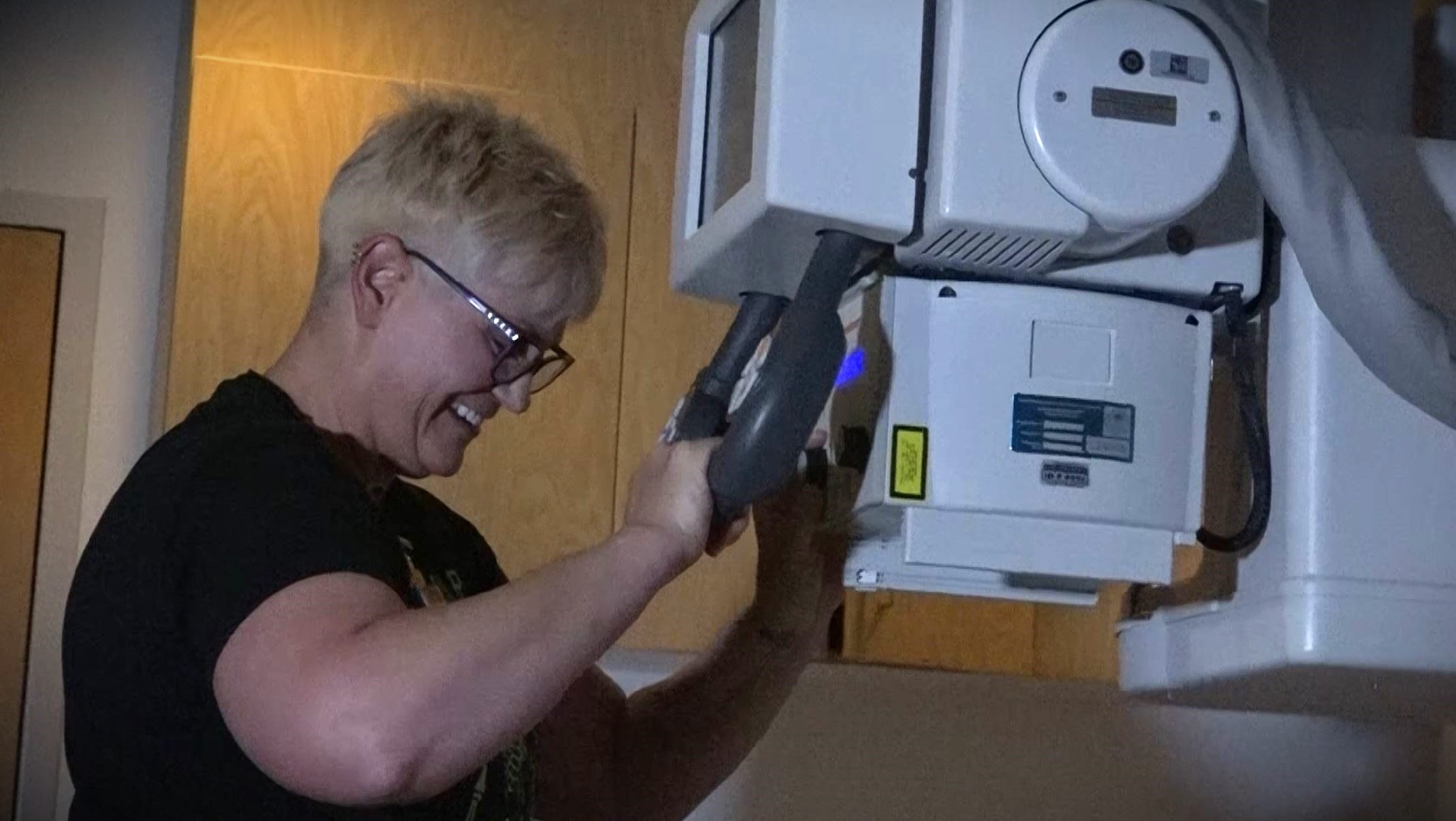 A person with short hair adjusts a medical imaging device in a clinical setting.
