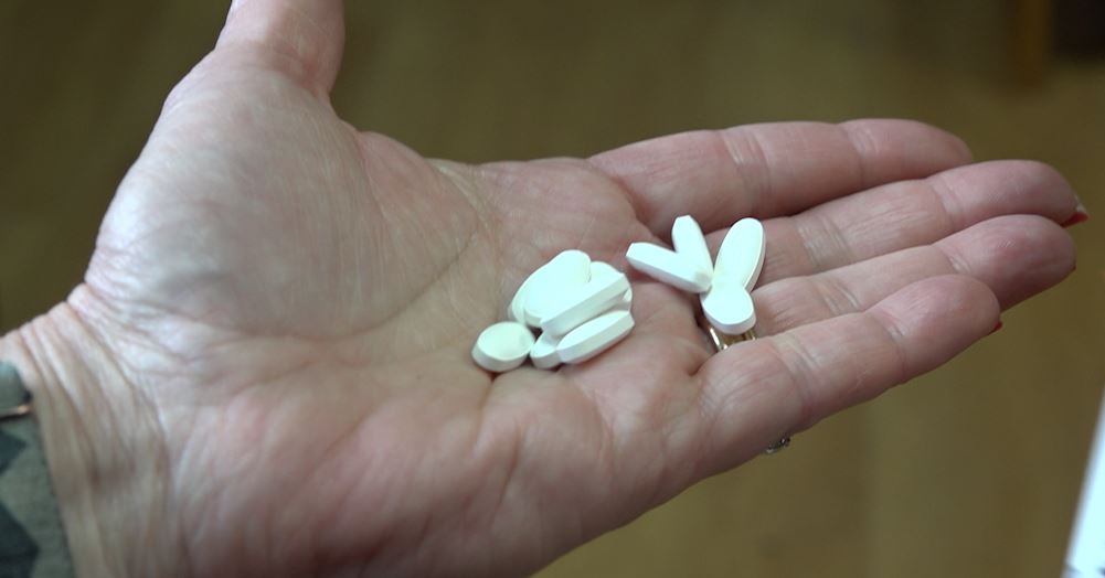 A hand holding several white oblong and oval pills.