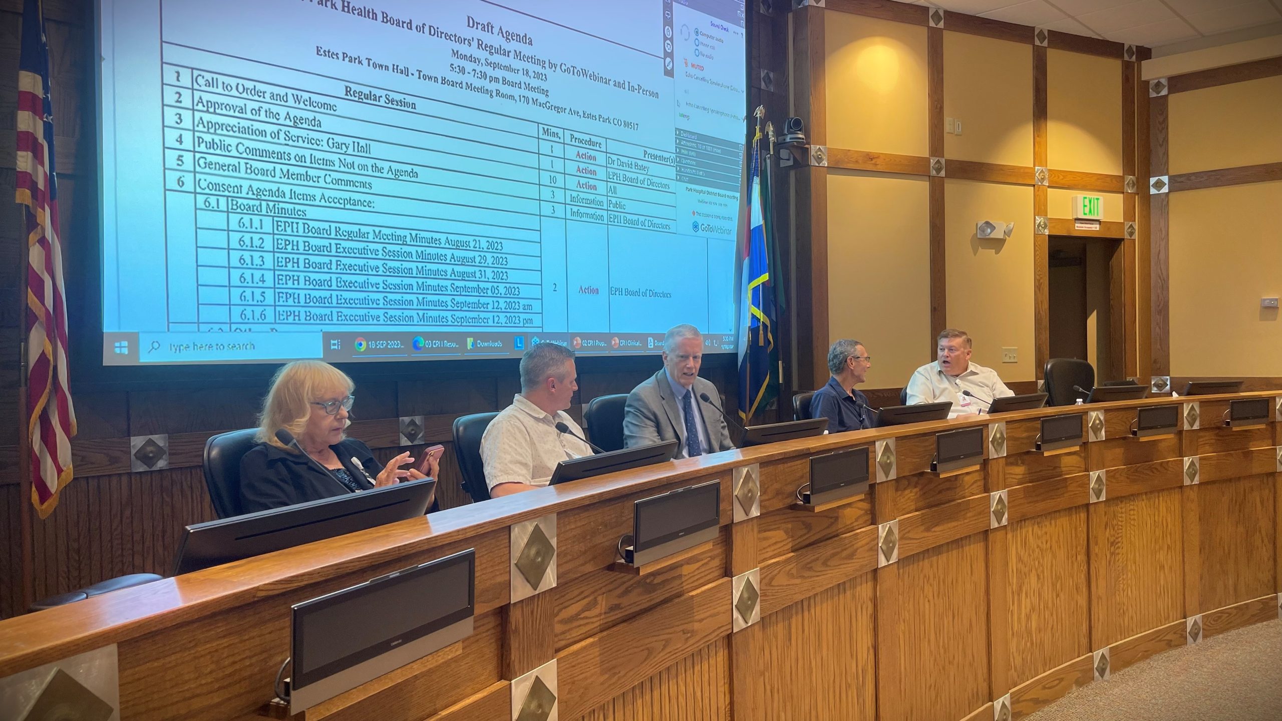 A group of officials seated at a long wooden desk in a meeting room. Projected on the screen behind them is an agenda for the Elko County Commission meeting.