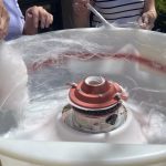 Two people are making cotton candy using a cotton candy machine. Their hands are visible as they spin the sugar onto sticks inside the machine's bowl.