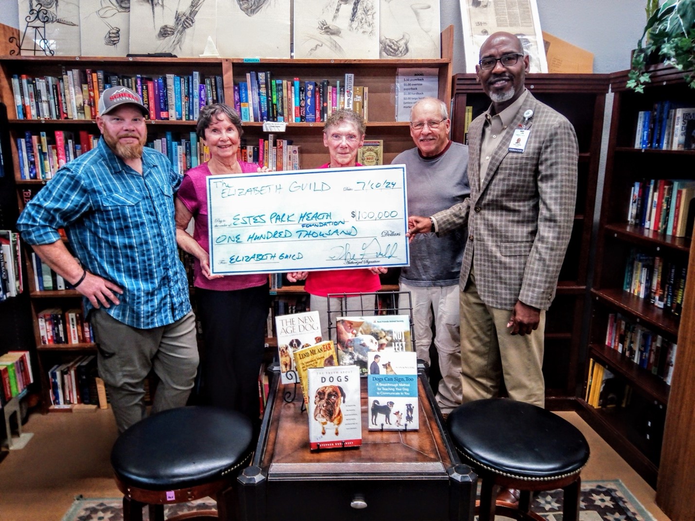 Five people stand in a bookstore, holding a large ceremonial check for $100,000 made out to 