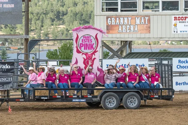 A group of people in pink shirts sits on a trailer float at a rodeo event, with a large 