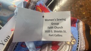 A label reads, "Women's Sewing Group, Faith Church, 3920 S. Shields St., Fort Collins," attached to a piece of fabric with colorful patterns.