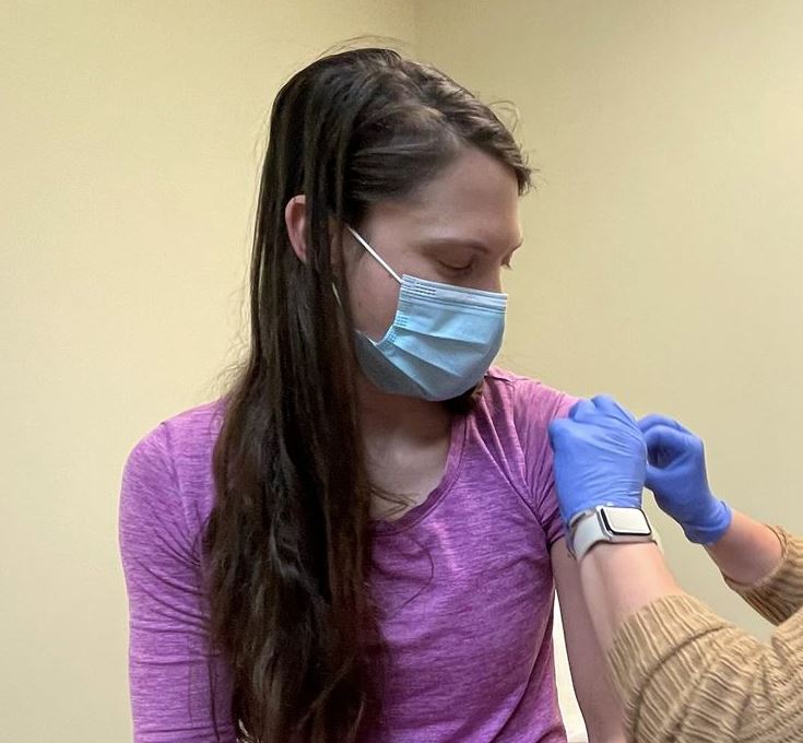 A person wearing a mask receives a vaccination from a healthcare worker wearing gloves.