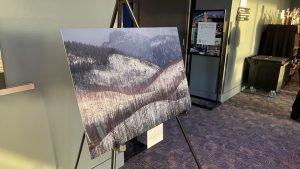 A photo of a snowy, forested landscape on an easel in a room, with a winding road visible.