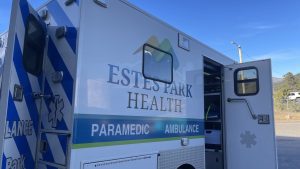 Ambulance from Estes Park Health with open rear door, parked in a lot under a clear sky.