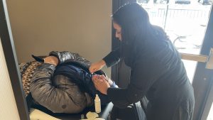 A person receives an eyebrow threading service from a technician in a salon.