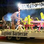 A parade float titled "Bigfoot Barbecue" features a large figure in a brown furry suit and green figures sitting at a picnic table, with the sign "Welcome, Out-of-Towners.