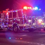 A fire truck decorated with colorful lights drives down a street at night during a parade.