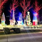 A festive holiday parade float with decorated gnome-shaped objects, illuminated by lights. A sign reads "Gnome for the Holidays.