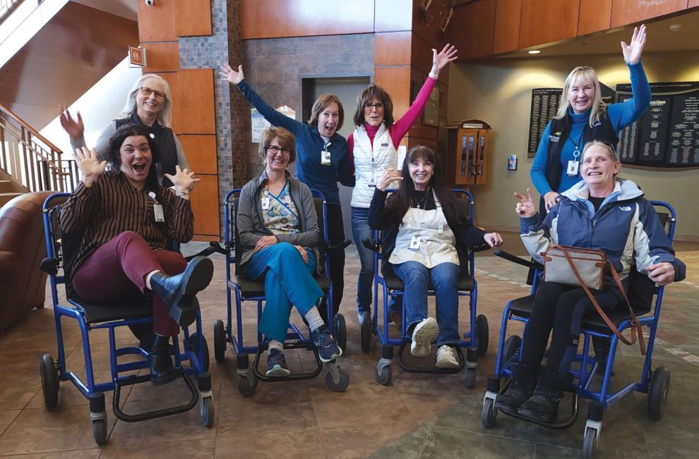 Eight people, some sitting in wheelchairs, pose happily with raised arms in a spacious lobby area.