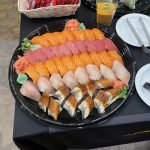 A black platter with assorted sushi, including salmon, tuna, and eel, garnished with wasabi, ginger, and sprouts.