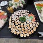 A platter of sushi rolls is arranged on a table, surrounded by other dishes.