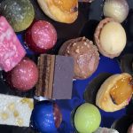 An assortment of colorful pastries, chocolates, and cakes on a dark plate.