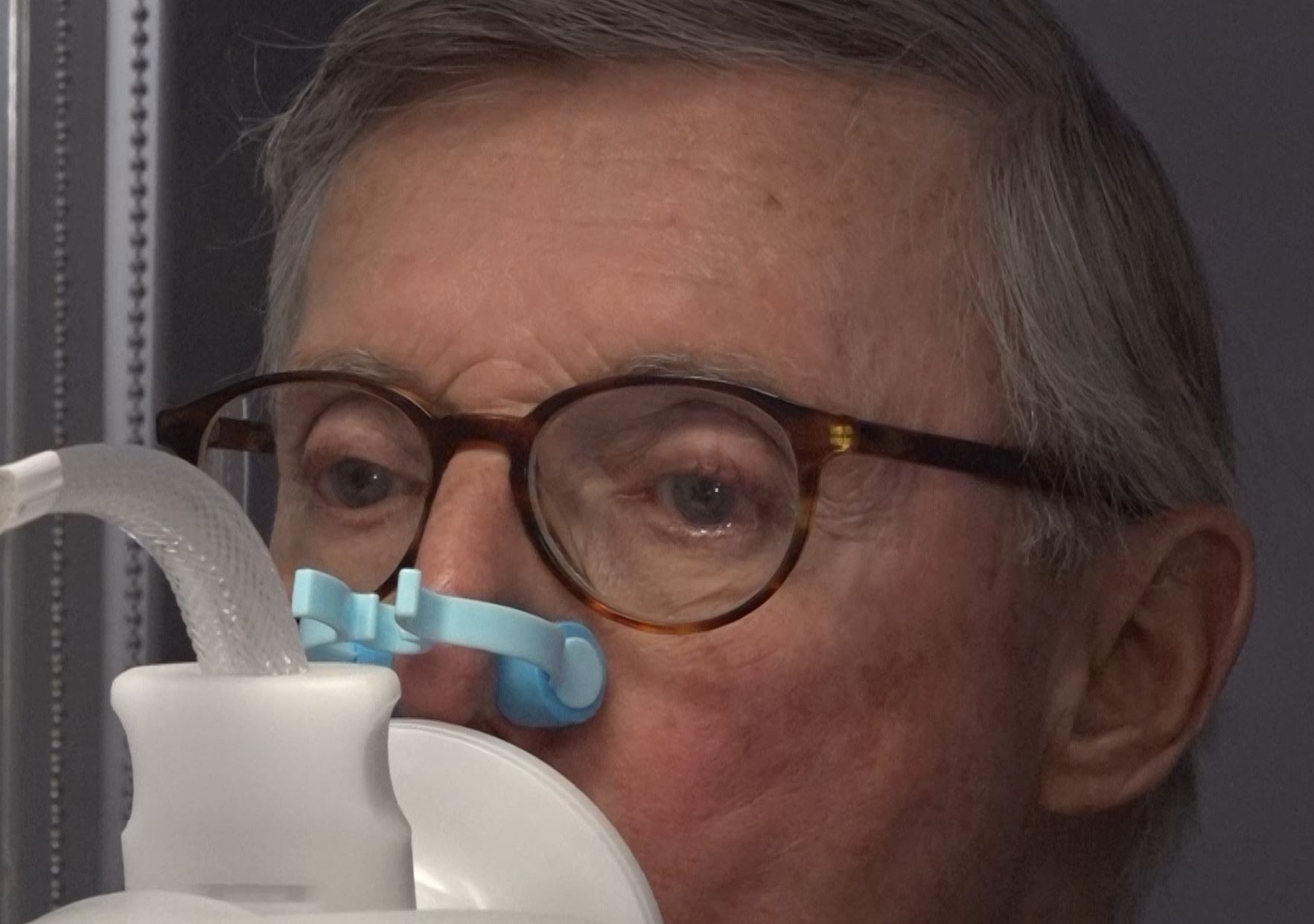 Person with glasses using a respiratory device, with a blue clip on their nose.