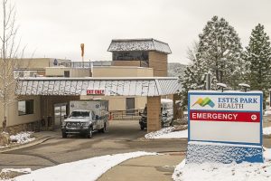 An ambulance is parked under a covered entrance at Estes Park Health Emergency, with snow on the ground and rooftops.