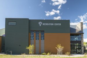Modern two-story building with "Recreation Center" sign, large windows, and minimal landscaping, under a clear blue sky with scattered clouds.