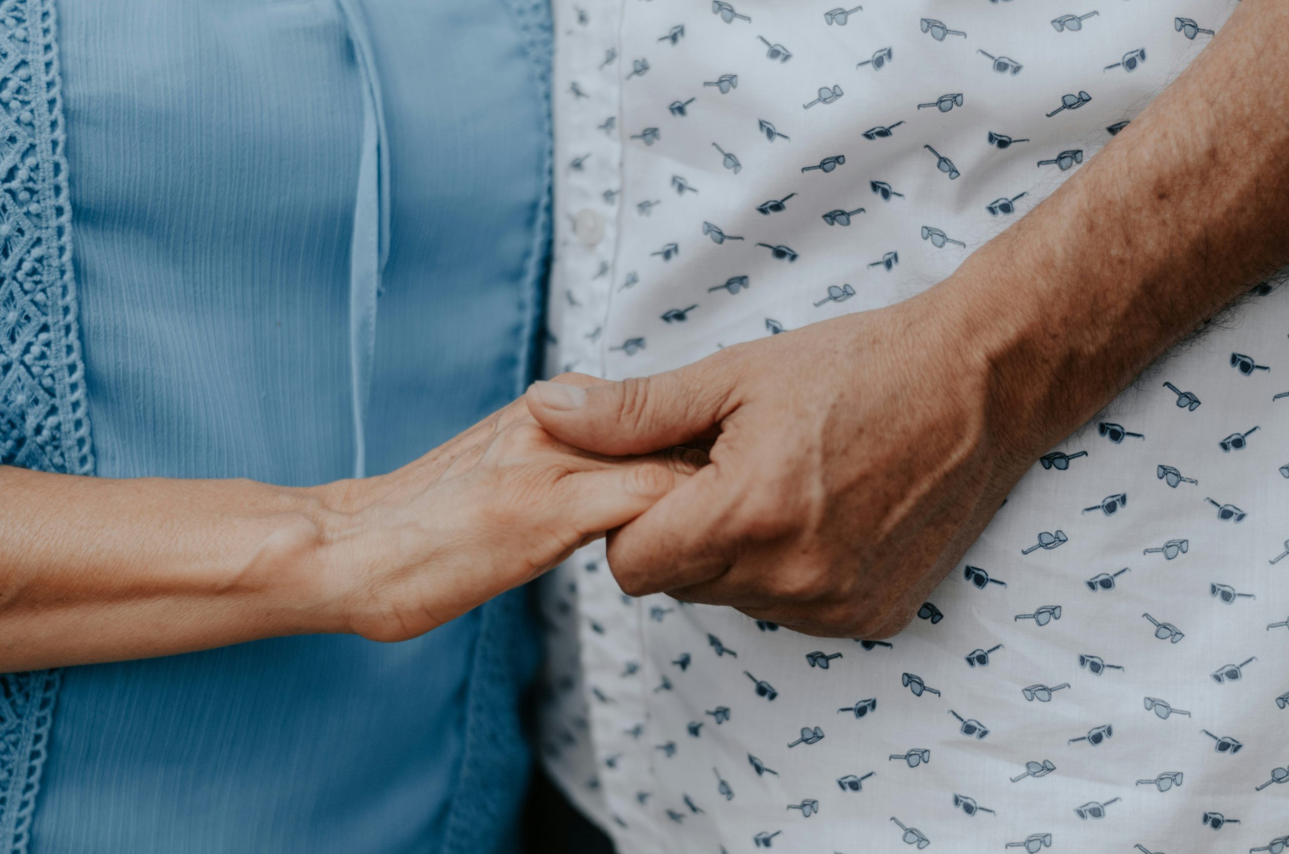 Two people holding hands; one person wearing a light blue shirt, the other wearing a white shirt with a pattern.